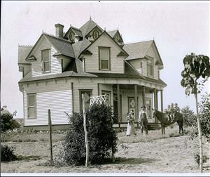 The Gallaher family -- a man, a woman holding a baby, and three young children stting on horse -- in front of a multi-gabled Victorian-style house in Bridgeport. 