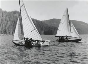 Black and white photo of two sailboats on a lake with young men on board both boats