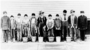 A row of Native American boys in work clothes with buckets and scrub brushes