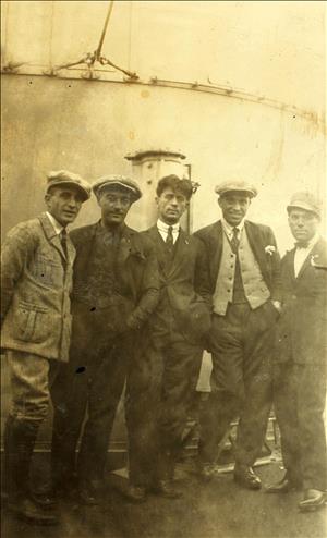 Four men in caps and wool suits standing in front a steel structure