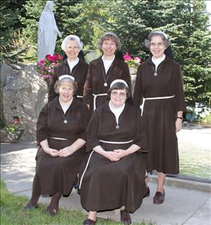 Five white women in brown nuns habits posing in a garden