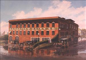 A three story brick building with many arched windows. Horse drawn wagons parked in front. Blue sky with clouds above. 