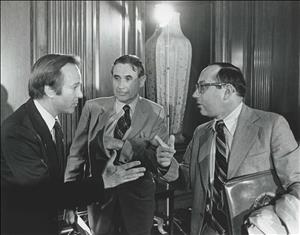 Three white men in suits talking to each other and gesturing