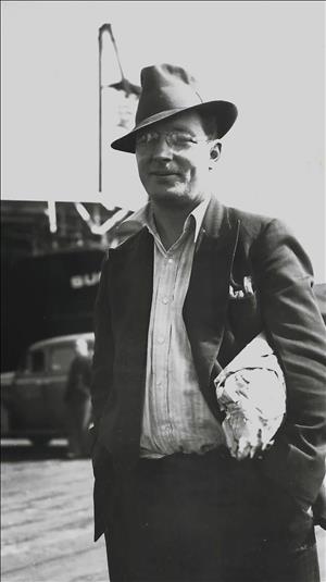A white man in hat and glasses carries a parcel under his arm