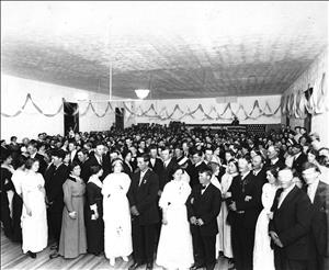 Formally dressed couples pose on dance floor, filling a large hall draped with bunting 