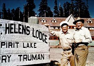 Two white men smiling next to a sign in front of a lodge