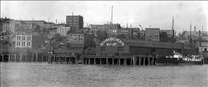Building on a dock in Seattle with a curved roof reading "Schwabacher's Wharf"