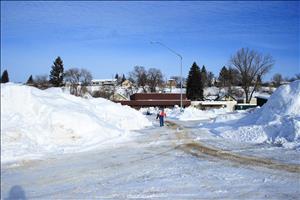 A lone man walks down an icy street in Spokane with snow piled much higher than his head on both sides of the road