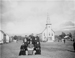 Nine white priests sit in a field with a church in the background 