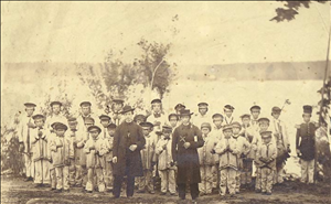 Two white priests pose in front of a large group of Native American boys of different ages