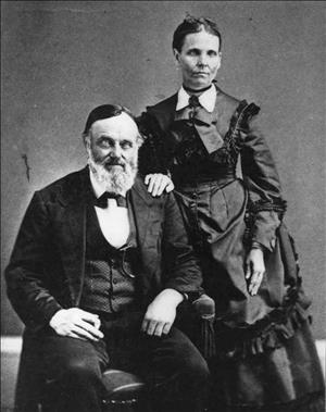 Nancy Bell stands in a dark, frilled dress with white collar with a hand placed on the shoulder of William Bell, seated in a vested suit