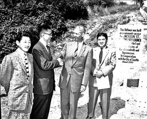 Luke shaking hands and smiling at the bottom of a hillside beside the words "This pathway was built as a community space by Jackson St. Community Council...Local residents and business in cooperation with the City of Seattle August 27, 1957"