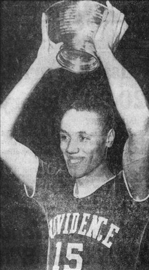 Wilkens smiling in a Providence University Jersey holding a trophy above his head with both arms