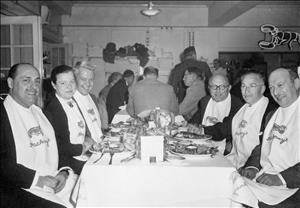 Morgan smiling at a table cloth covered table with five other diners wearing full body bibs reading Hackney's