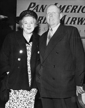 Beck and his wife in a patterned dress and hat in front of a banner reading Pan American Airway