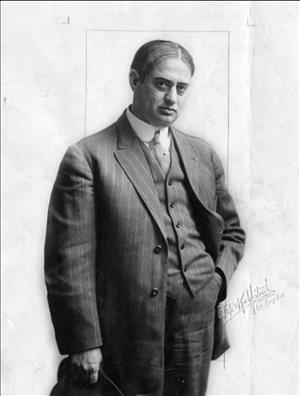 Pantages posing in a three piece suit, holding a hat