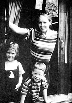 A woman in a striped shirt with two children smiling in a boat with a trailing wake in the background
