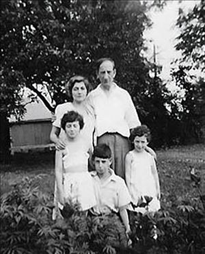 A family of five posing outside in white clothes in front of low foliage
