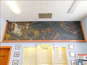 Mural of fishermen trawling in two boats mounted between the ceiling and wall of a room with one burnt out fluorescent light and three plaques that are titled, "Charters of Freedom"