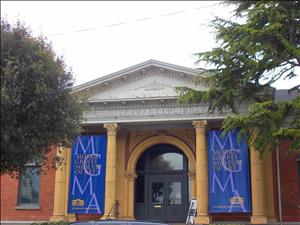 A neoclassical brick building with roman pediment reading "Carnegie Free Library" leading to ionic columns painted yellow with two blue pendants reading "Morris Graves Museum of Art" between them