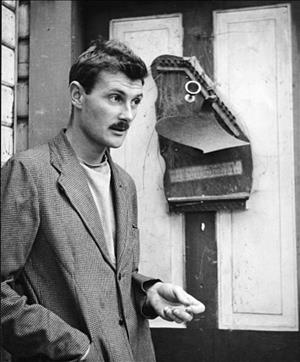 A young Graves in a plaid suit jacket and mustache in front of a door that damaged zither has been nailed into