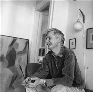 Cumming smiling, seated with one of his paintings visible in the background