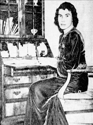 Virginia Bloedel seated at a desk in front of stationary in a dark velvet or silk dress