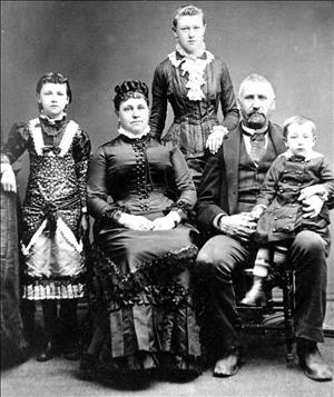Family of five posing in ornate, dark Victorian formal wear