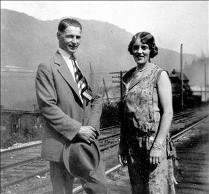 A couple standing in front of railroad tracks wearing semi-formal wear and smiling