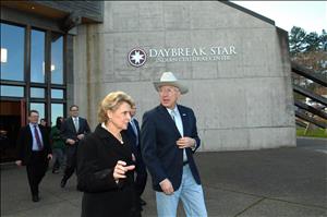 Gregoire speaking and walking beside a man wearing a cowboy hat and bolo tie, exiting a building that reads, "Daybreak Center, Indian Cultural Center"