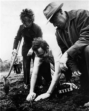 Three people kneeling and leaning. One person has their hands in the dirt, They are all smiling.