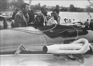 Three people stand beside a hydroplane with an ornate, white exhaust pipe