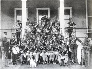 Several rows of men in military uniform holding band instruments and standing on the steps of a building