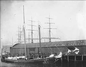 Ship moored at a dock in front of a building reading "Schwabacher Bros. & Co. Wholesale Grocery"
