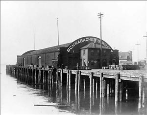 Building on a dock with a curved roof reading "Schwabacher's Wharf"