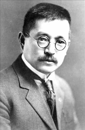 Person in a suit and tie in round glasses and short cropped hair posing while seated